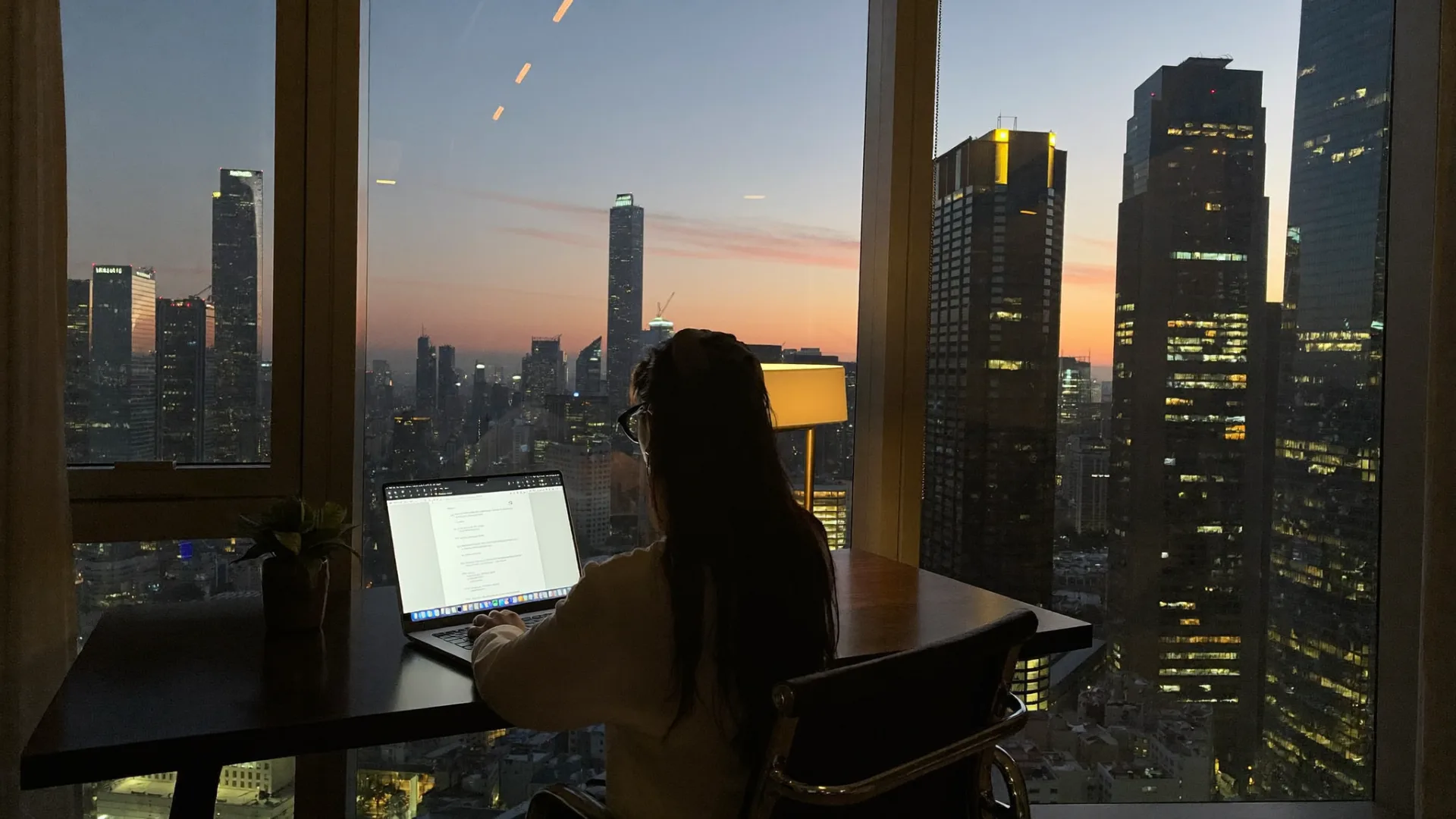 Corporate guest working at a desk with a city skyline view in a Trade Nest Stays apartment